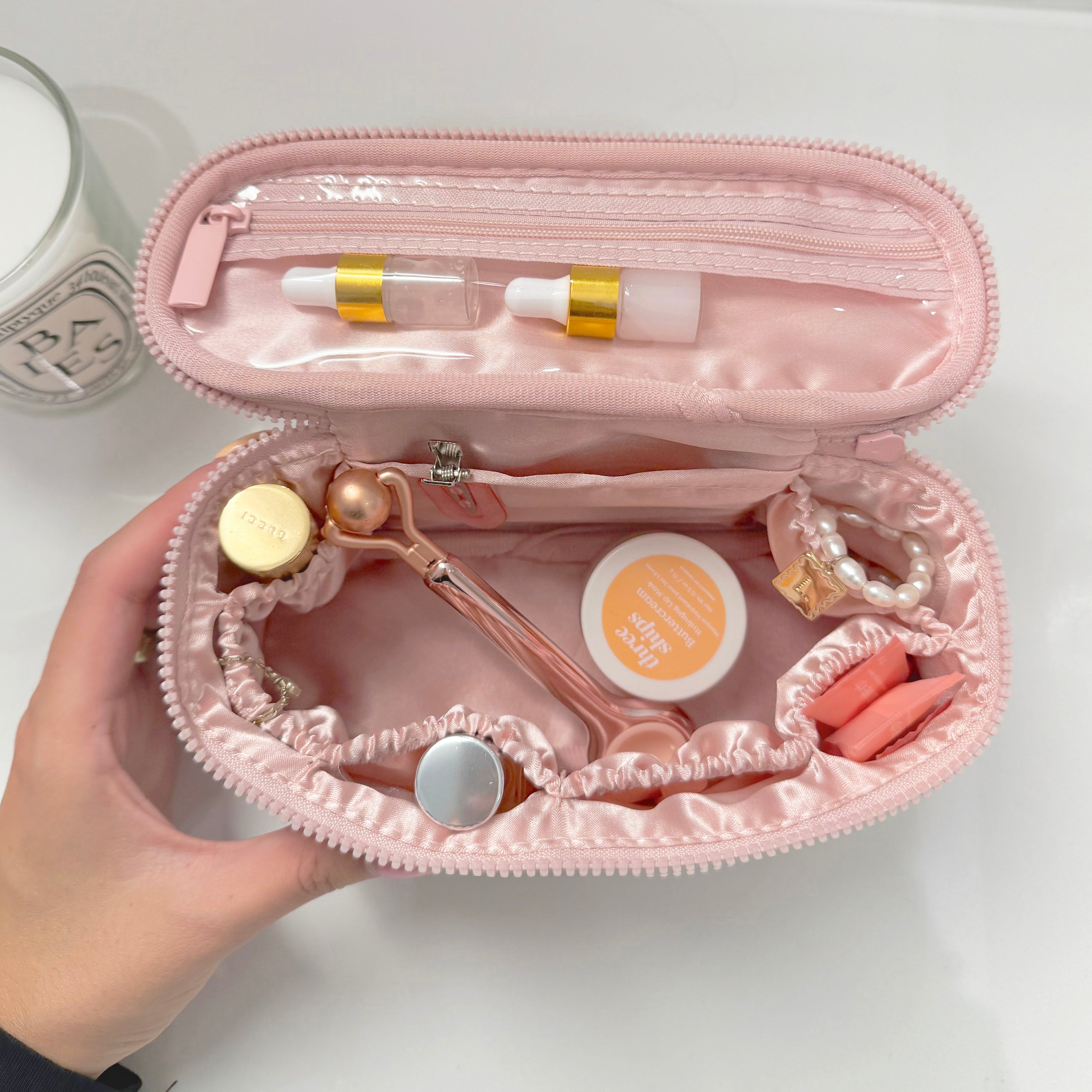Pink jewelry case with various items including earrings and makeup held by a hand.