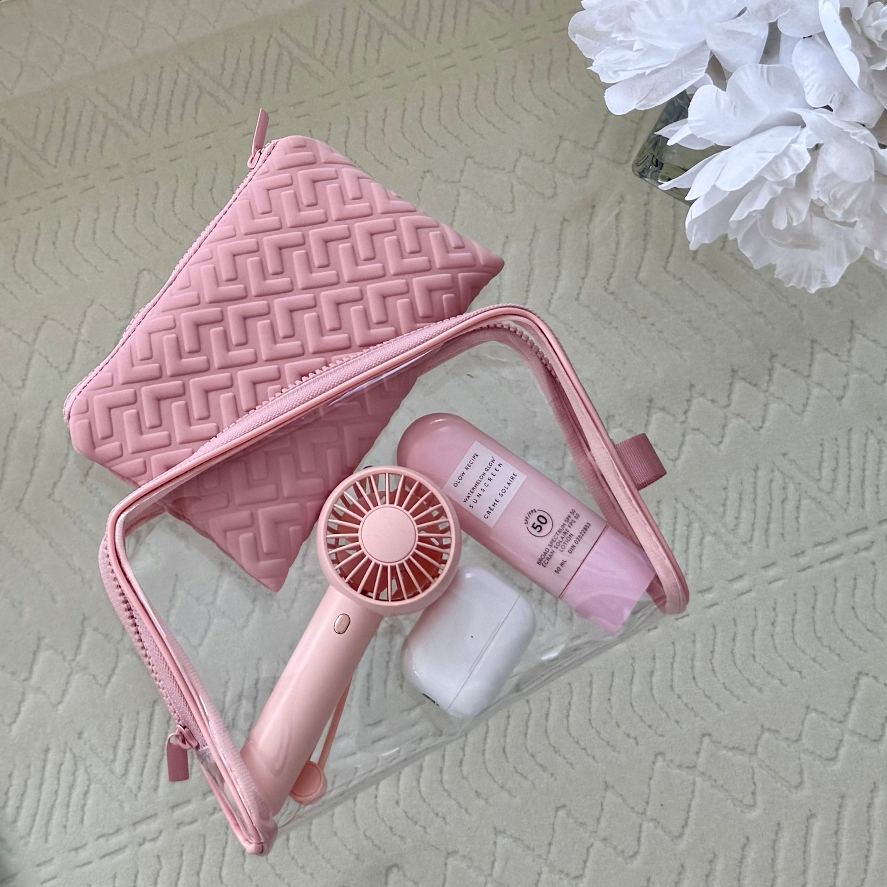 Pink travel set with mirror, hair dryer, and bottle on a textured surface.